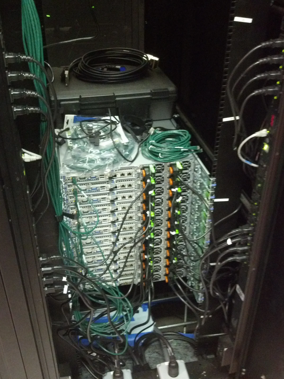 Ein Serverschrank mit zahlreichen grünen und schwarzen Kabeln, die an die Geräte angeschlossen sind.